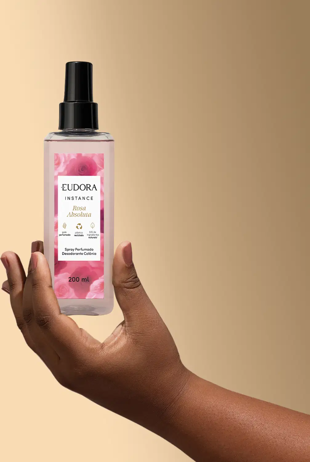 Mão segurando o frasco do Spray Perfumado Instance Rosa Absoluta. Um franco de plástico e transparente, com a tampa preta.