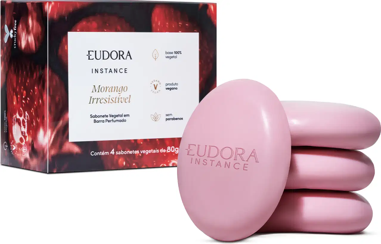O produto apresentado é um conjunto de sabonetes vegetais da marca Eudora Instance, com fragrância de morango irresistível. A embalagem consiste em uma caixa vermelha e preta, contendo 4 sabonetes em formato oval de cor rosa.