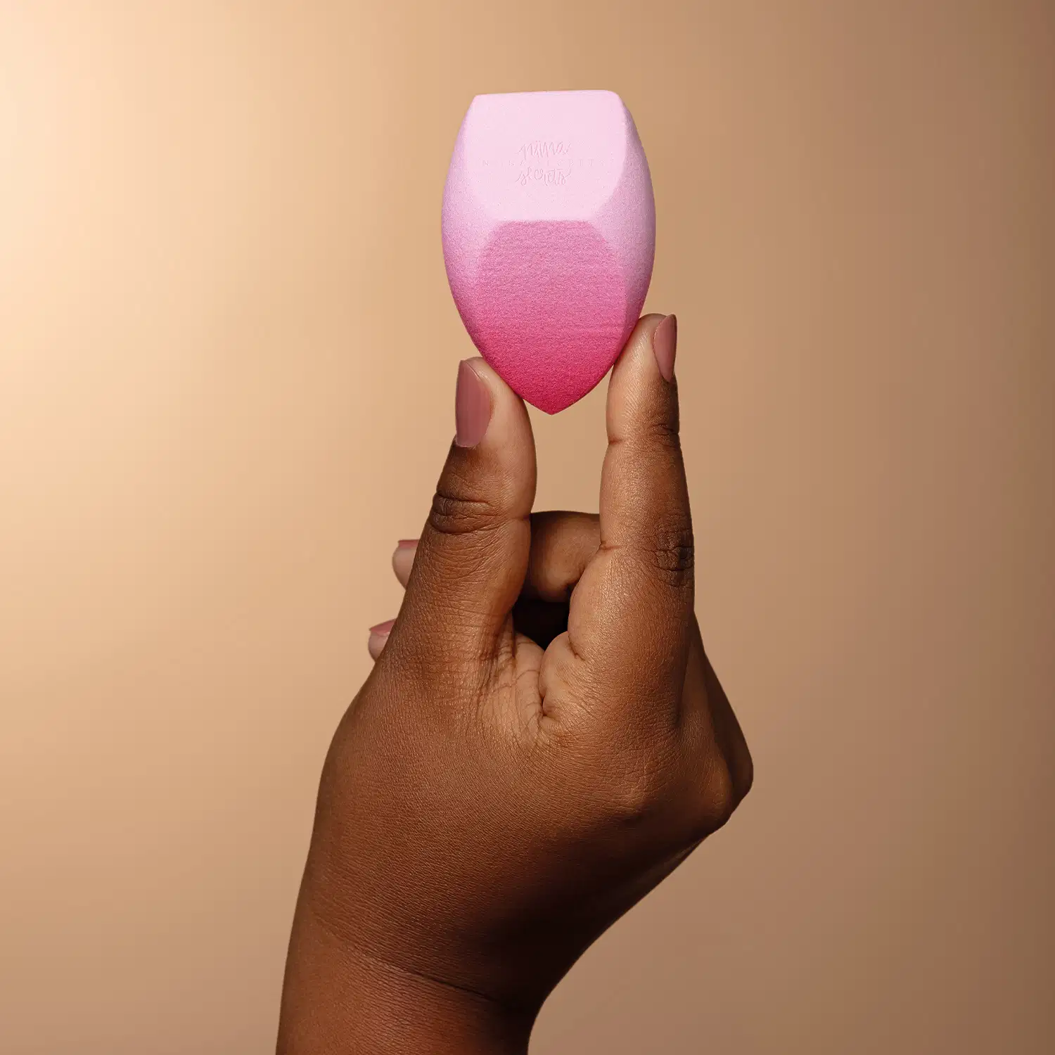 Mão feminina segurando na ponta dos dedos a Esponja Pink Blend Niina Secrets.