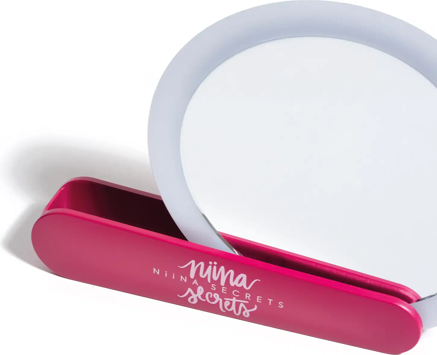 O produto apresentado é um espelho de maquiagem da marca Niina Secrets. O espelho é redondo e possui uma borda branca ao redor. A alça giratória, de cor rosa, serve como suporte, para deixar o espelho apoiado.