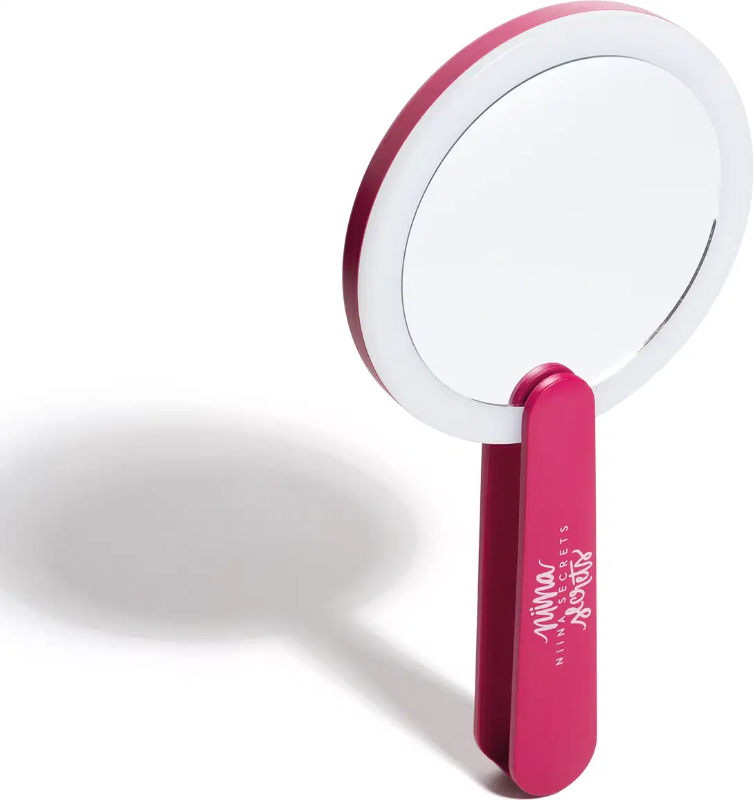 O produto apresentado é um espelho de mão da marca Niina Secrets. Possui um formato circular com um aro branco e um cabo de cor rosa vibrante. O nome da marca "Niina Secrets" está impresso no cabo do espelho em letras brancas.