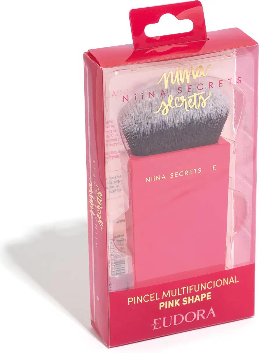 O produto apresentado é um pincel de maquiagem da marca Niina Secrets. O pincel possui cerdas macias e uma base em um tom rosa vibrante, com o nome da marca impresso em letras douradas. Na imagem, está dentro da embalagem de plástico e transparente.