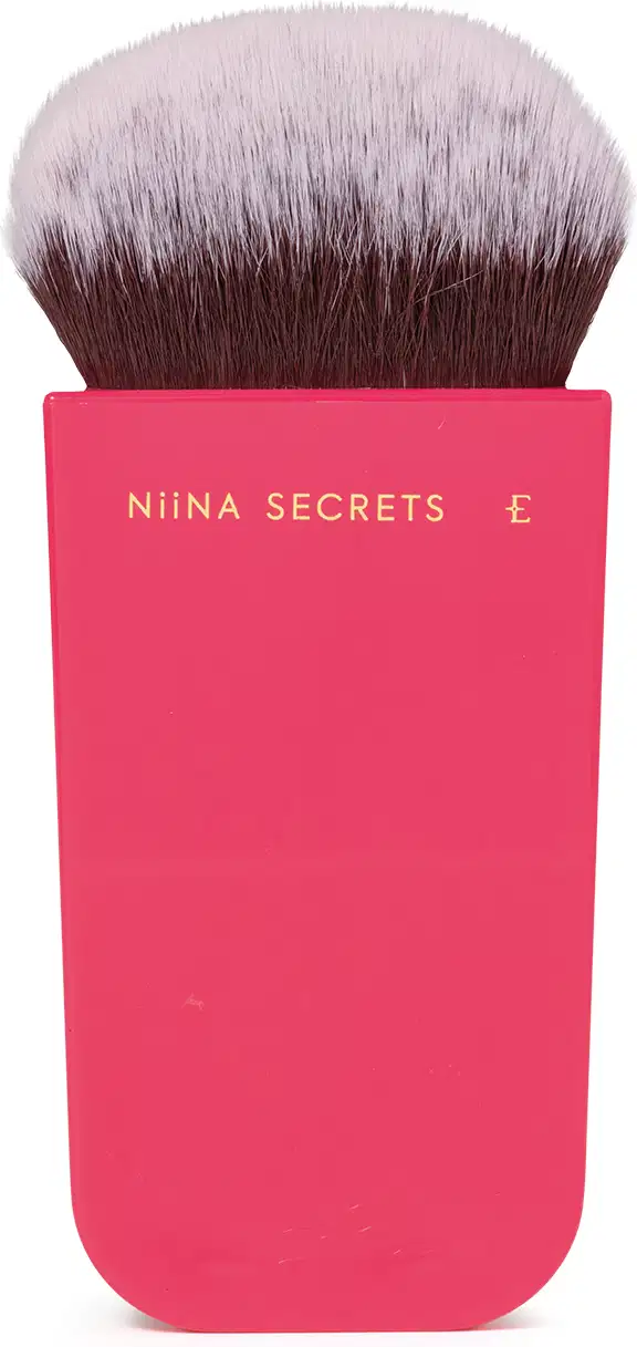 O produto apresentado é um pincel de maquiagem da marca Niina Secrets. O pincel possui cerdas macias e uma base em um tom rosa vibrante, com o nome da marca impresso em letras douradas.