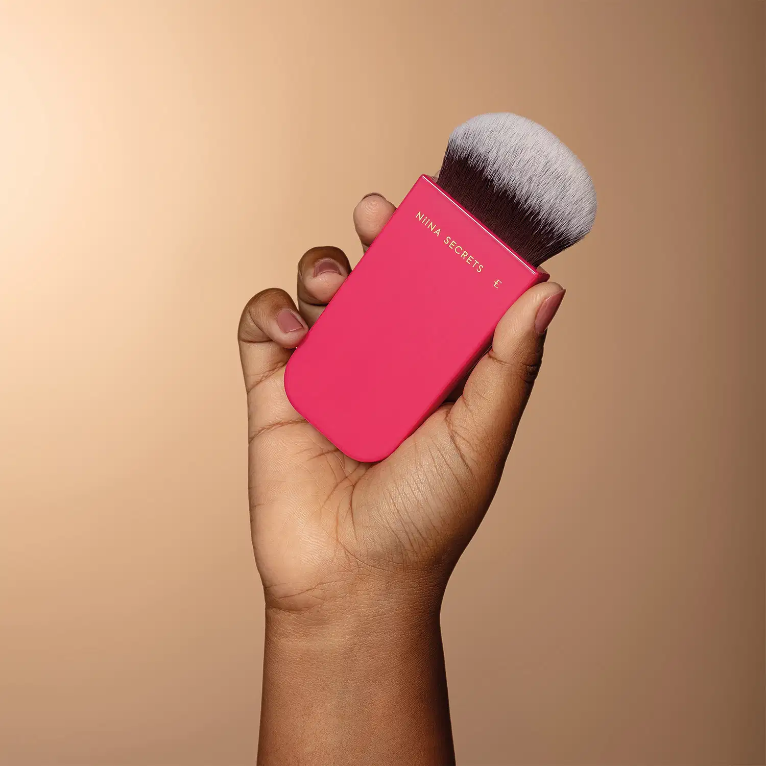 Pincel Multifuncional Pink Shape Niina Secrets sendo segurado por uma mão feminina.