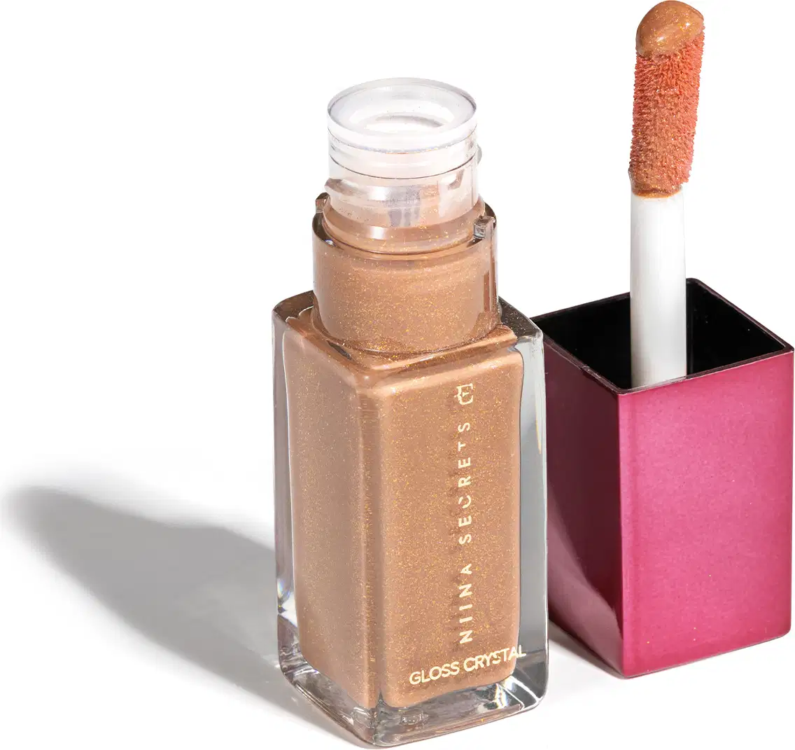 Frasco de cristal com gloss labial dourado da marca Niina Secrets, embalado em frasco de vidro, quadrado, transparente com tampa rosa. O produto apresenta um aplicador de espuma na ponta.