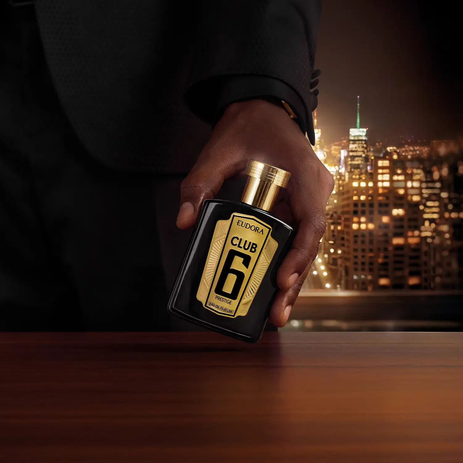 A mão segura um frasco de perfume da marca Club 6 em primeiro plano, com um cenário urbano iluminado ao fundo, sugerindo um ambiente elegante e sofisticado para o uso deste produto de beleza.