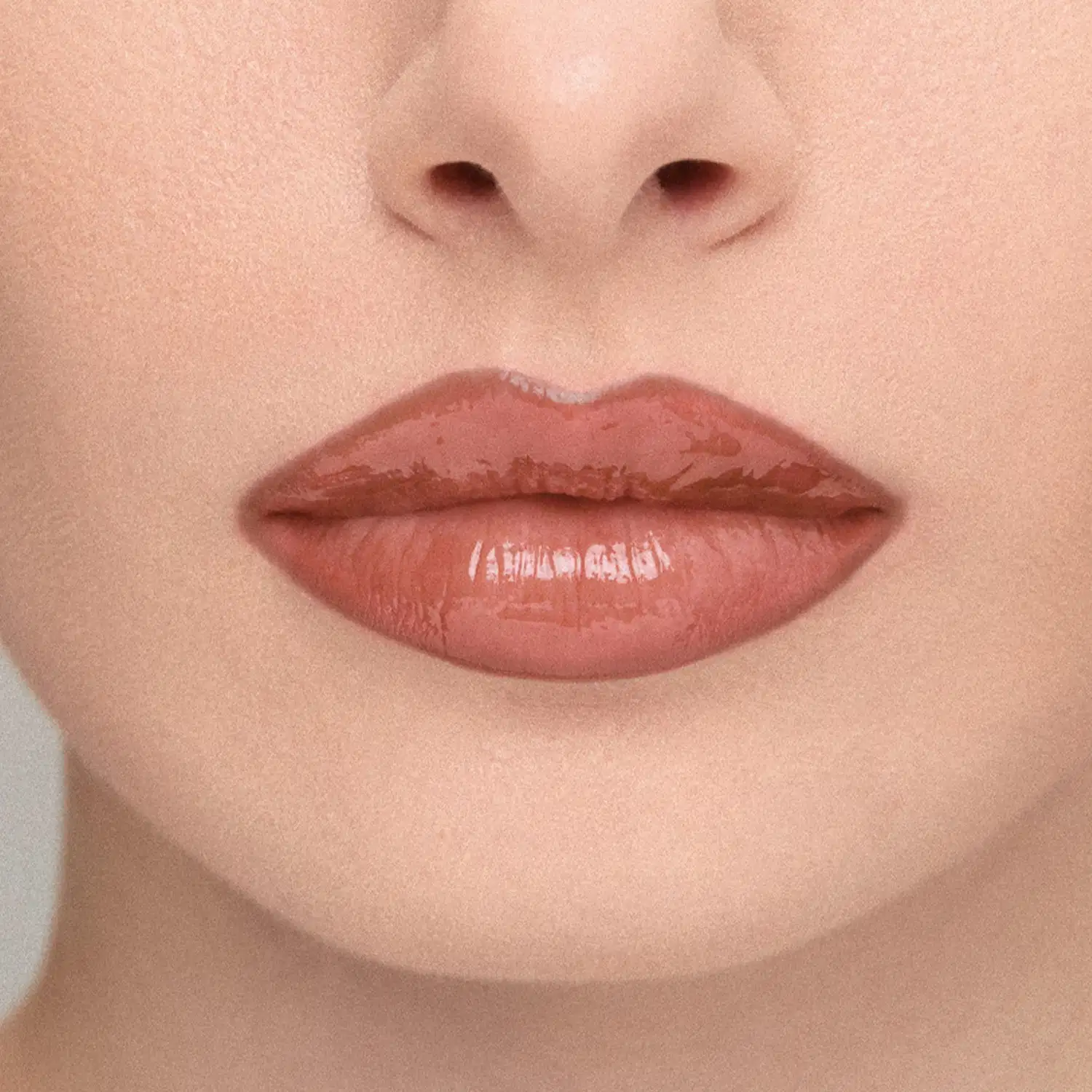 Imagem em close-up de lábios de uma modelo, mostrando o efeito do Gloss Labial: Lábios amarronzado com brilho, em primeiro plano, sobre fundo neutro.
