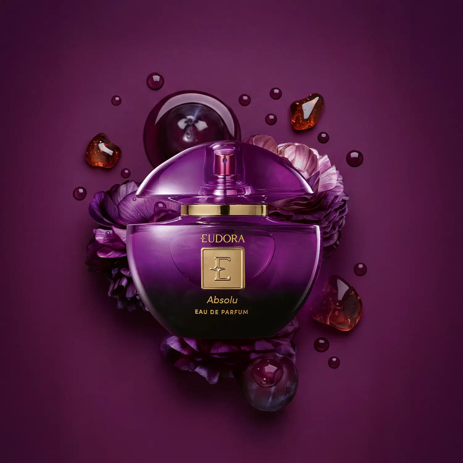 Frasco de perfume Eudora Absolu em tom roxo, com tampa dourada e rodeado por flores roxas e gotas de líquido âmbar. Embalagem elegante e sofisticada.