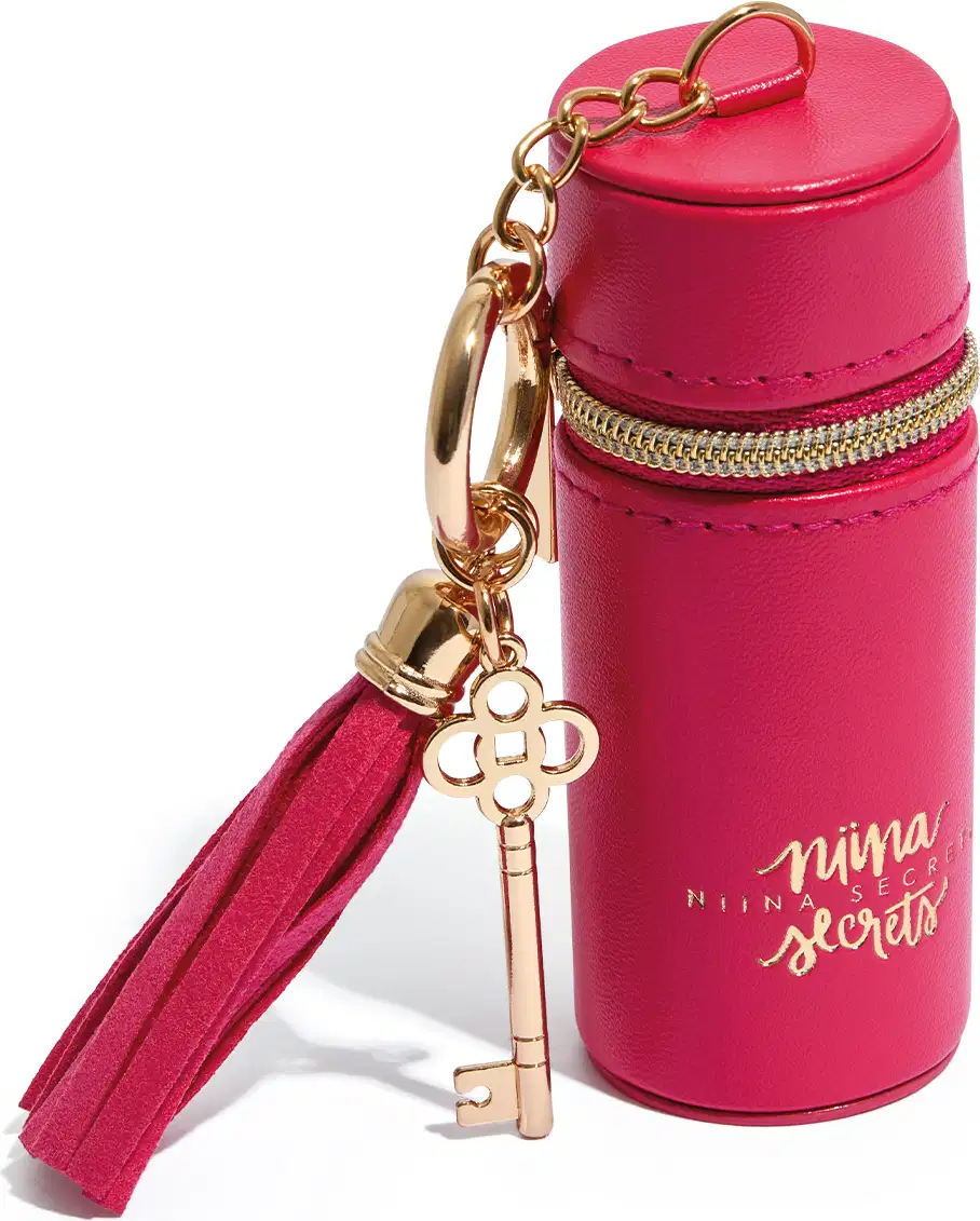 Acessório rosa em formato cilíndrico com zíper dourado, pingente em formato de chave e texto "Niina Secrets" impresso na embalagem.