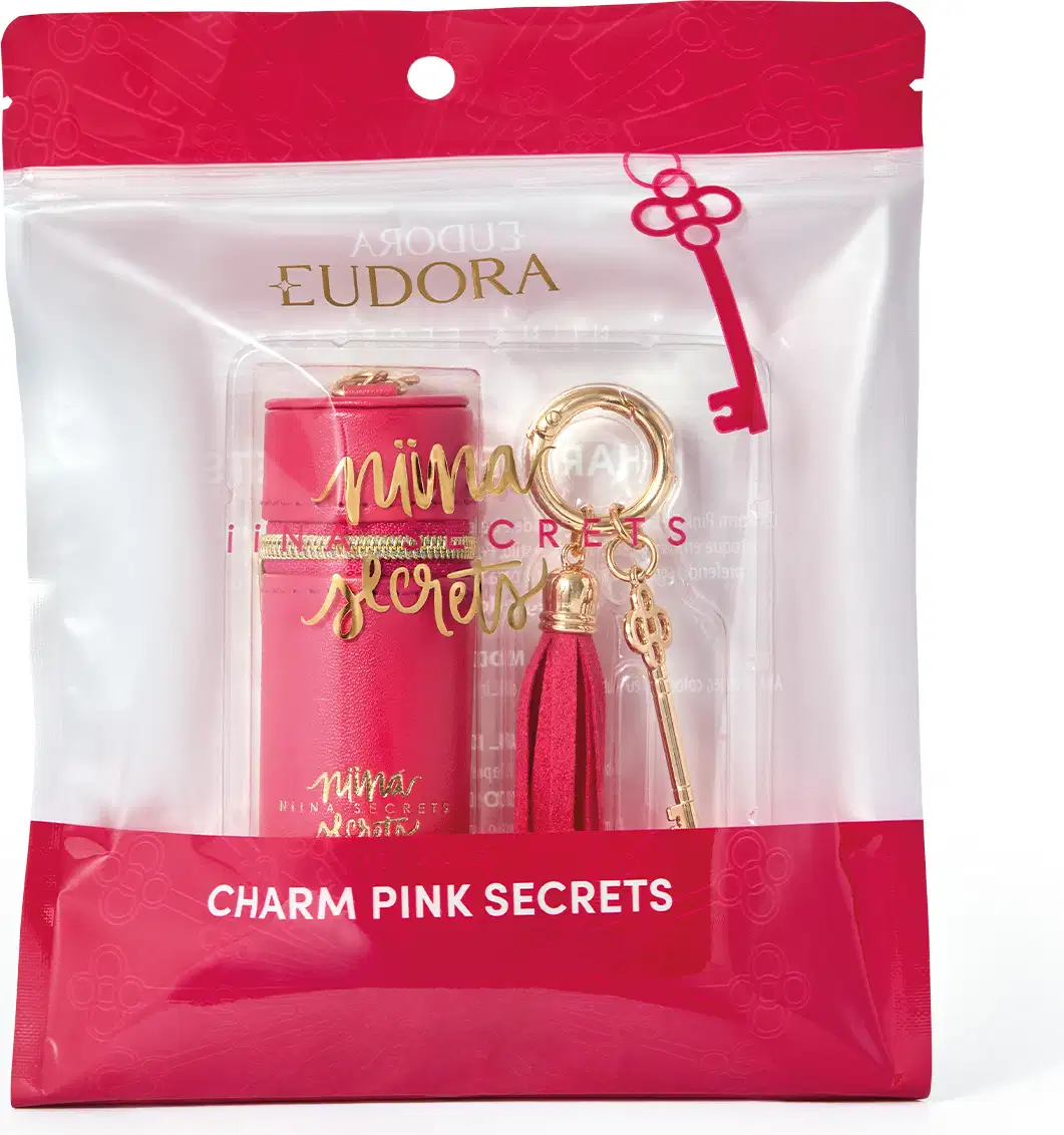 Embalagem rosa com detalhes dourados contendo um acessório da marca Niina Secrets, com pingente e borla decorativa.