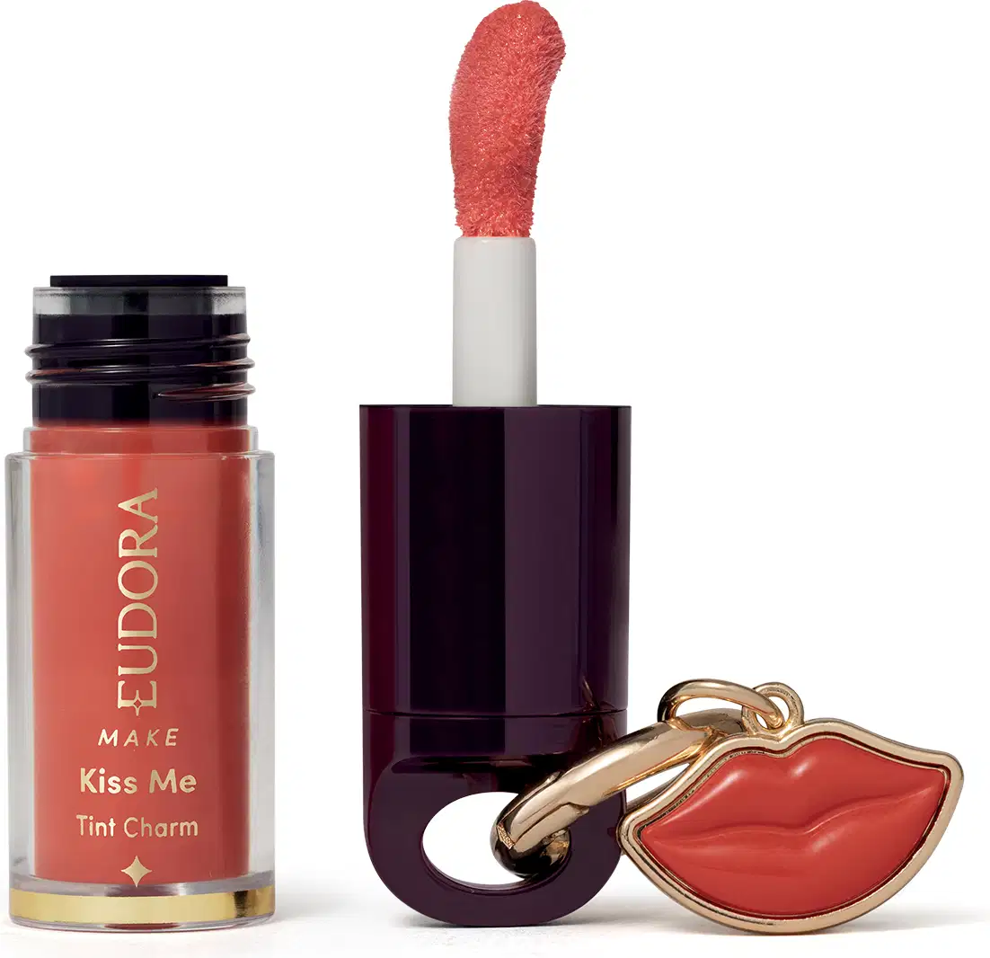 O produto de beleza Eudora Make apresenta um frasco de tinta labial na cor coral e um batom vermelho em embalagem preta com detalhes dourados, além de um pingente em formato de lábios.