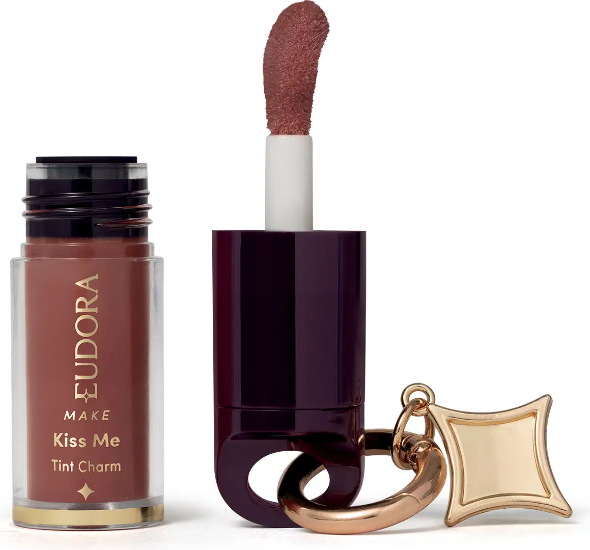 O produto de beleza Eudora Make é um batom líquido com acabamento cremoso na cor marrom avermelhado, em embalagem com frasco e aplicador. Possui rótulo com o nome "Kiss Me Tint Charm" e detalhes decorativos em dourado.