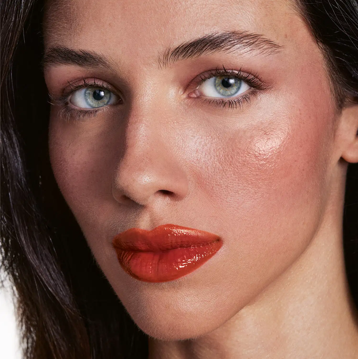 Retrato de uma mulher com maquiagem de alta qualidade, destacando seus olhos azuis e lábios vermelhos. A iluminação e o fundo escuro criam um ambiente elegante e sofisticado, sugerindo um contexto de produto de beleza de luxo.
