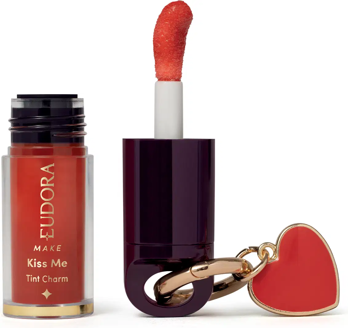 O produto de beleza Eudora Make é um batom líquido vermelho com acabamento brilhante, em embalagem cilíndrica preta e branca, acompanhado de um pingente em forma de coração vermelho.