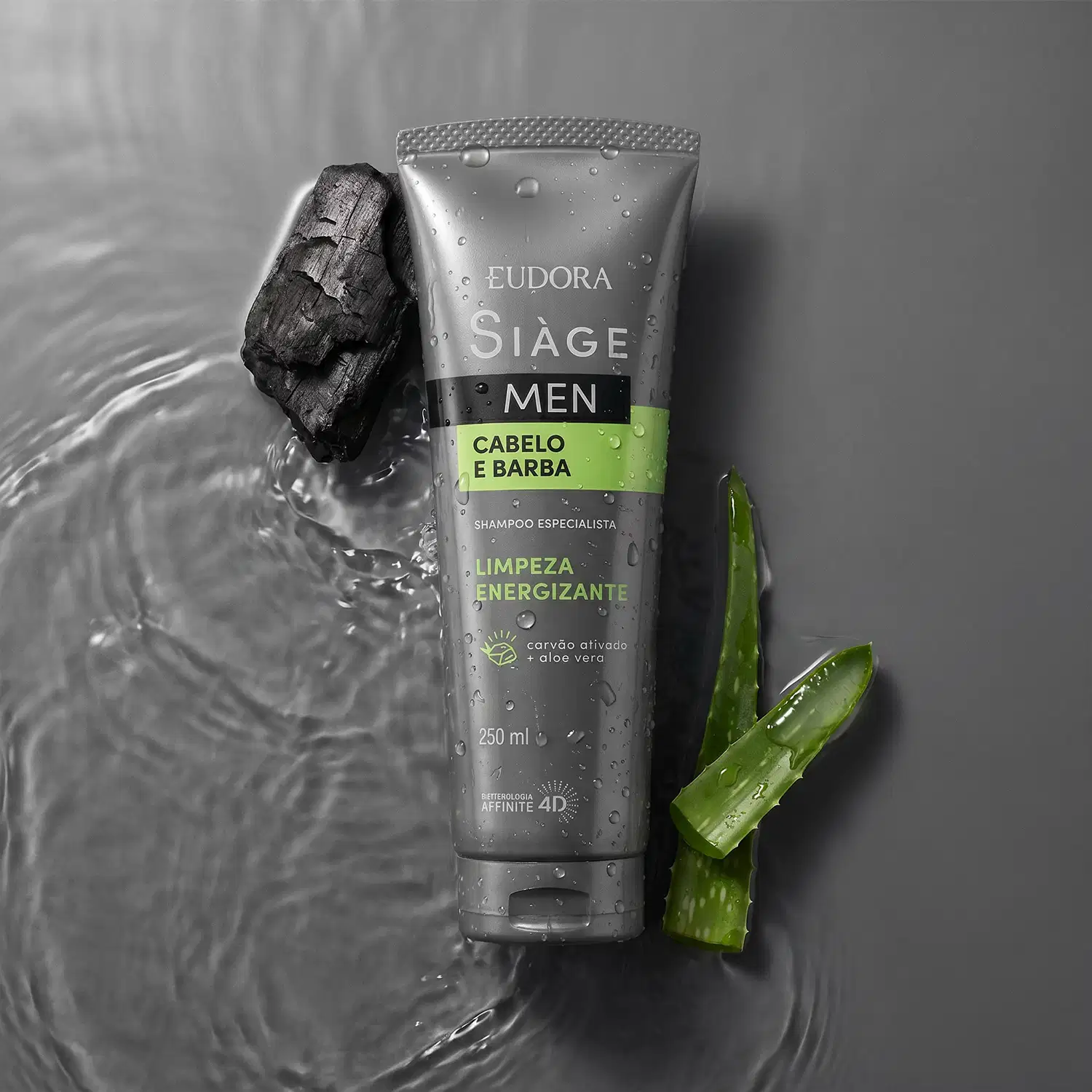 Tubo de shampoo da marca Siàge Men sobre superfície úmida com pedaço de carvão e folha de aloe vera ao redor, em tons de cinza e verde.