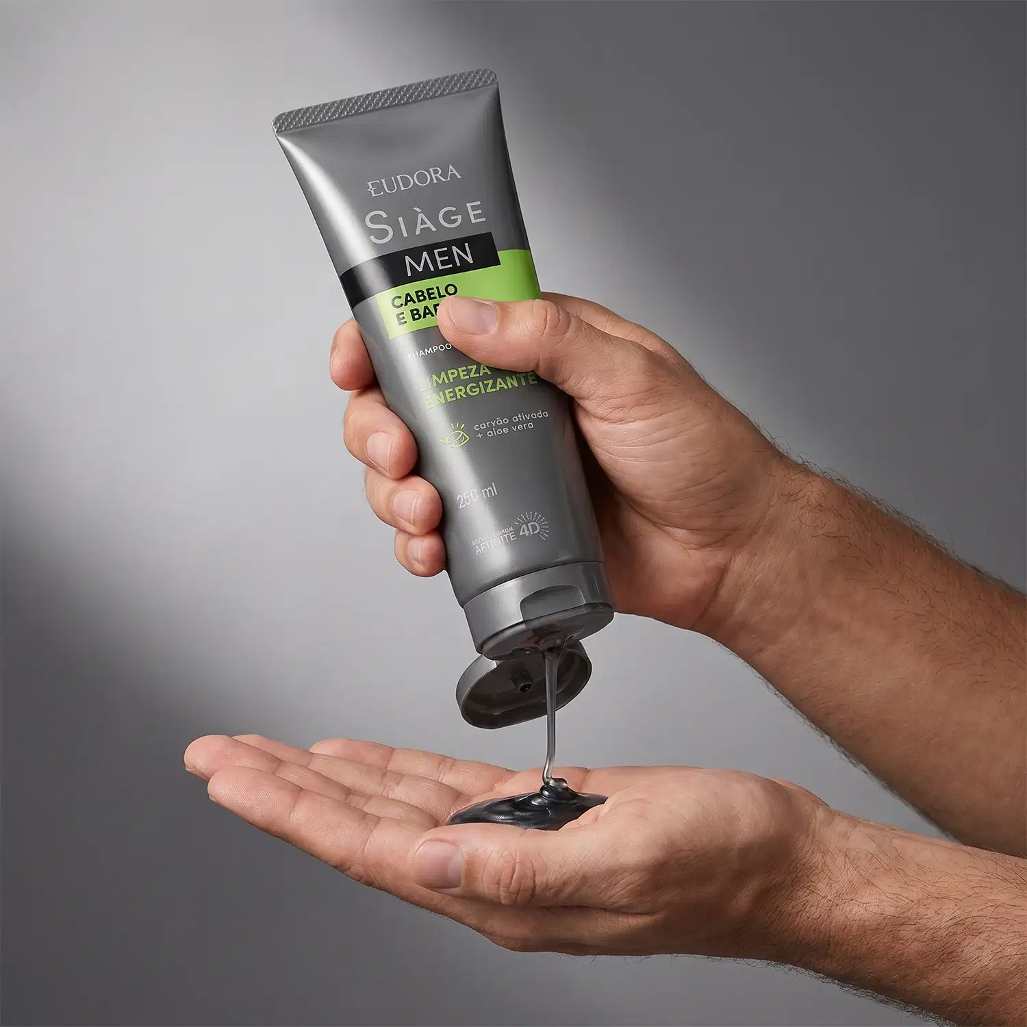 Tubo de shampoo da marca Siàge Men em mãos masculinas sobre fundo cinza, com textura líquida e embalagem visíveis.