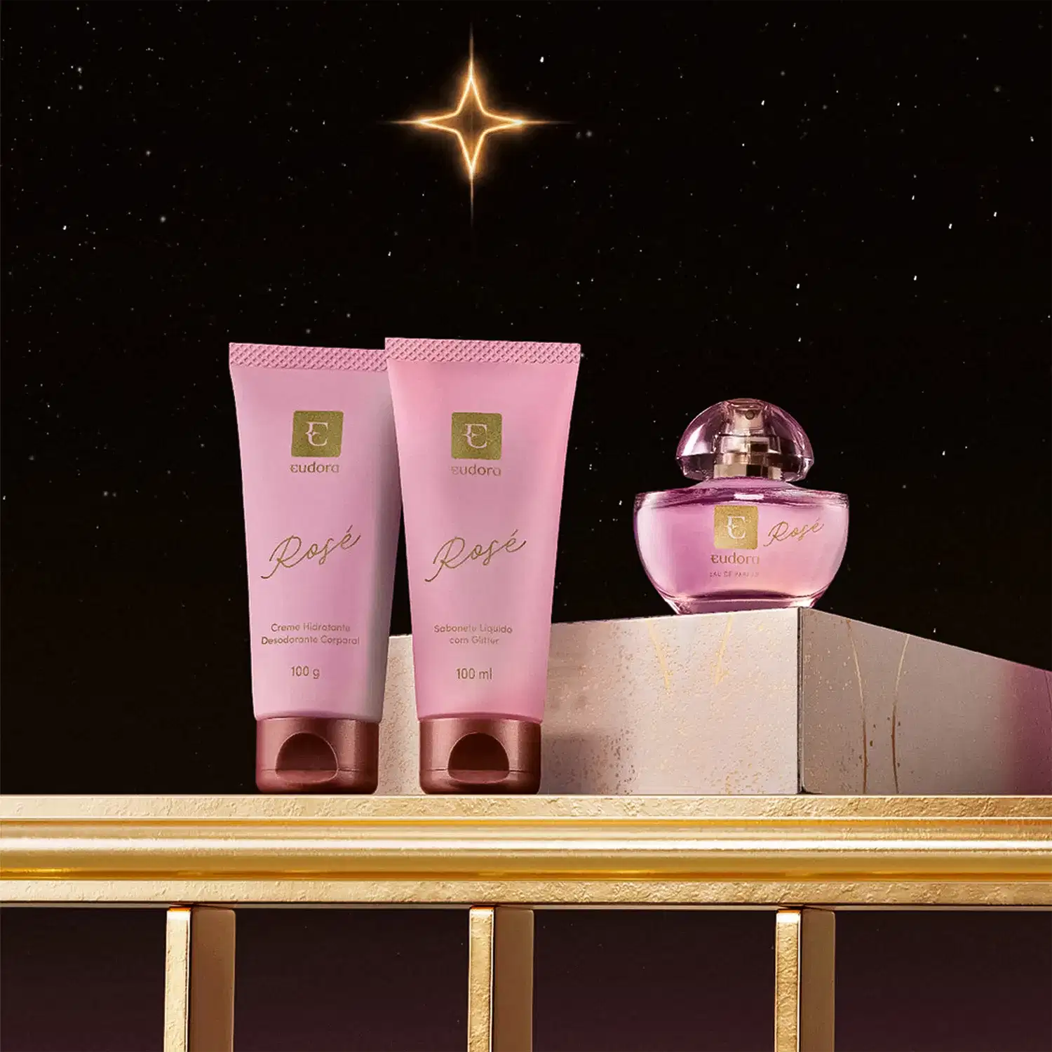 Linha Rosé Eudora composta por dois tubos rosa de 100g e 100ml com detalhes em ouro, e frasco de perfume rosa com tampa espelhada. Embalagem elegante com logotipo Eudora em dourado.