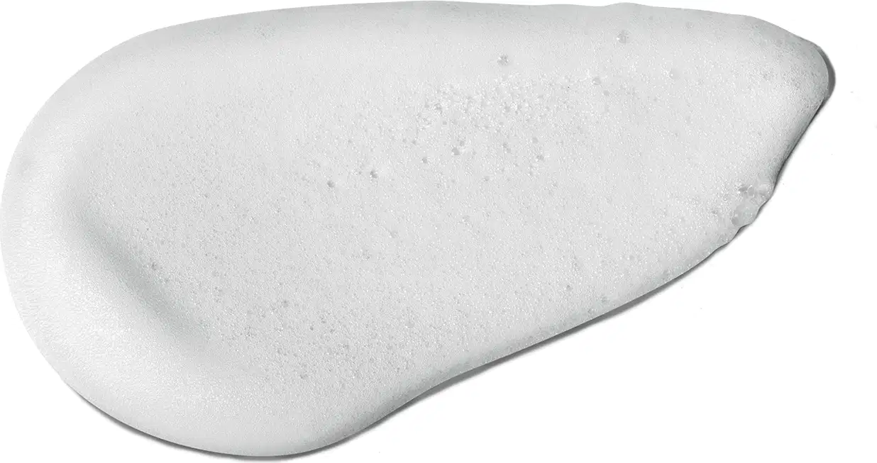 O produto apresenta uma textura suave, cremosa e uniforme, com uma aparência espumosa e brilhante. Sua superfície é areada, com pequenas bolhas visíveis. A cor predominante é o branco.