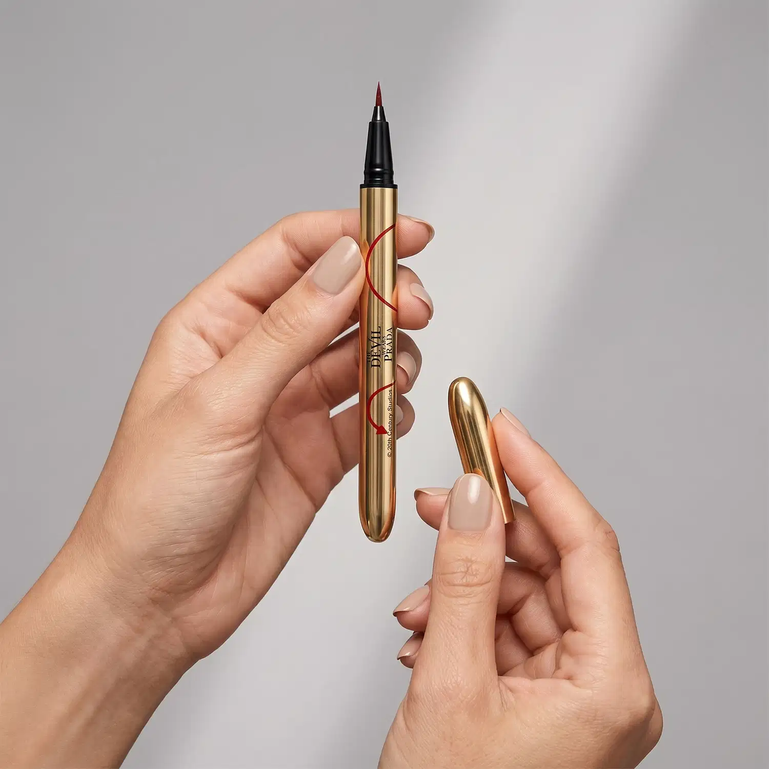 Imagem de um produto de maquiagem da marca Dior, um delineador líquido dourado com ponta fina, sendo segurado por mãos femininas com unhas pintadas em tons claros, em um fundo neutro e minimalista.