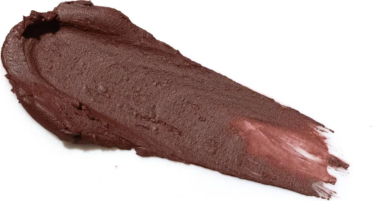 Amostra de batom amarronzado com textura cremosa e acabamento semi-matte. Apresenta superfície lisa e uniforme, com leve reflexo. A cor predominante é um tom de marrom profundo.