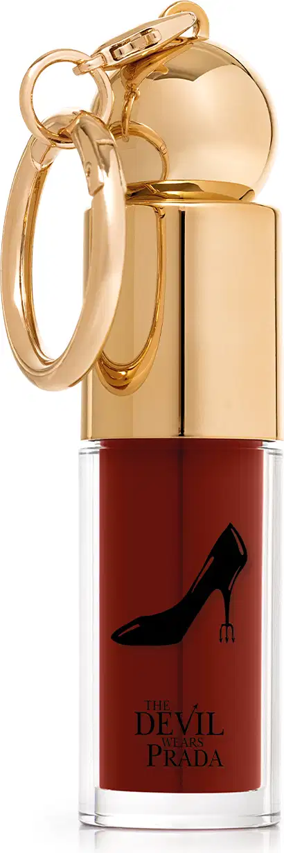 Embalagem do batom líquido, com tampa dourada e cor da make vermelho cereja. No rótulo, escrito: "The Devil Wears Prada" e imagem de um sapato de salto preto.
