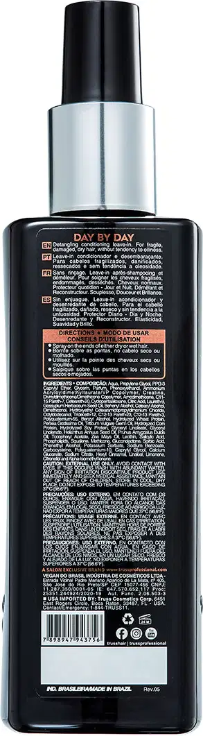 A imagem mostra um frasco plástico preto com uma tampa prateada. É um produto para cabelos chamado "Day by Day". O rótulo na parte traseira do frasco contém informações detalhadas sobre o produto, como instruções de uso, ingredientes e avisos.