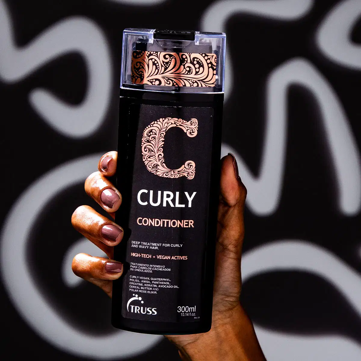 A imagem mostra uma mão segurando um frasco de condicionador da marca Truss, linha Curly. Também é possível ver o seu conteúdo, que é cremoso e branco, com 300ml.