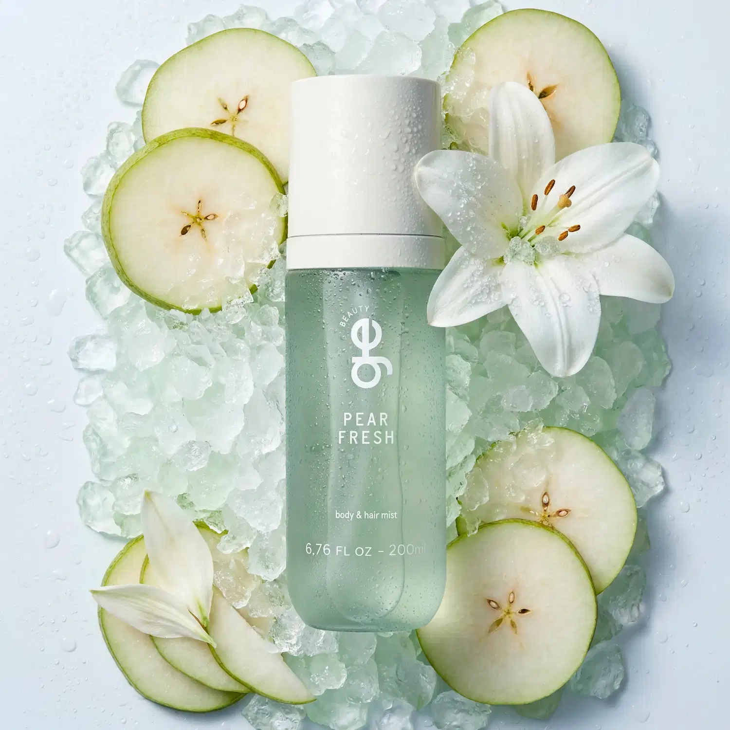 Spray corporal e capilar GE Beauty "Pear Fresh", frasco de 200 ml na cor verde-menta translúcida com tampa branca. Cercado por gelo, fatias de pera e uma flor de lírio branca.