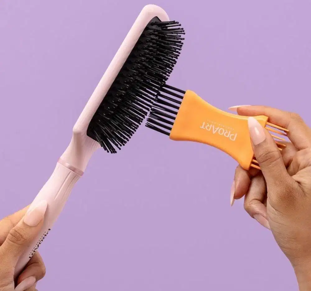 A imagem mostra uma mão feminina segurando uma escova e outra utilizando o limpador de escovas nas cerdas.