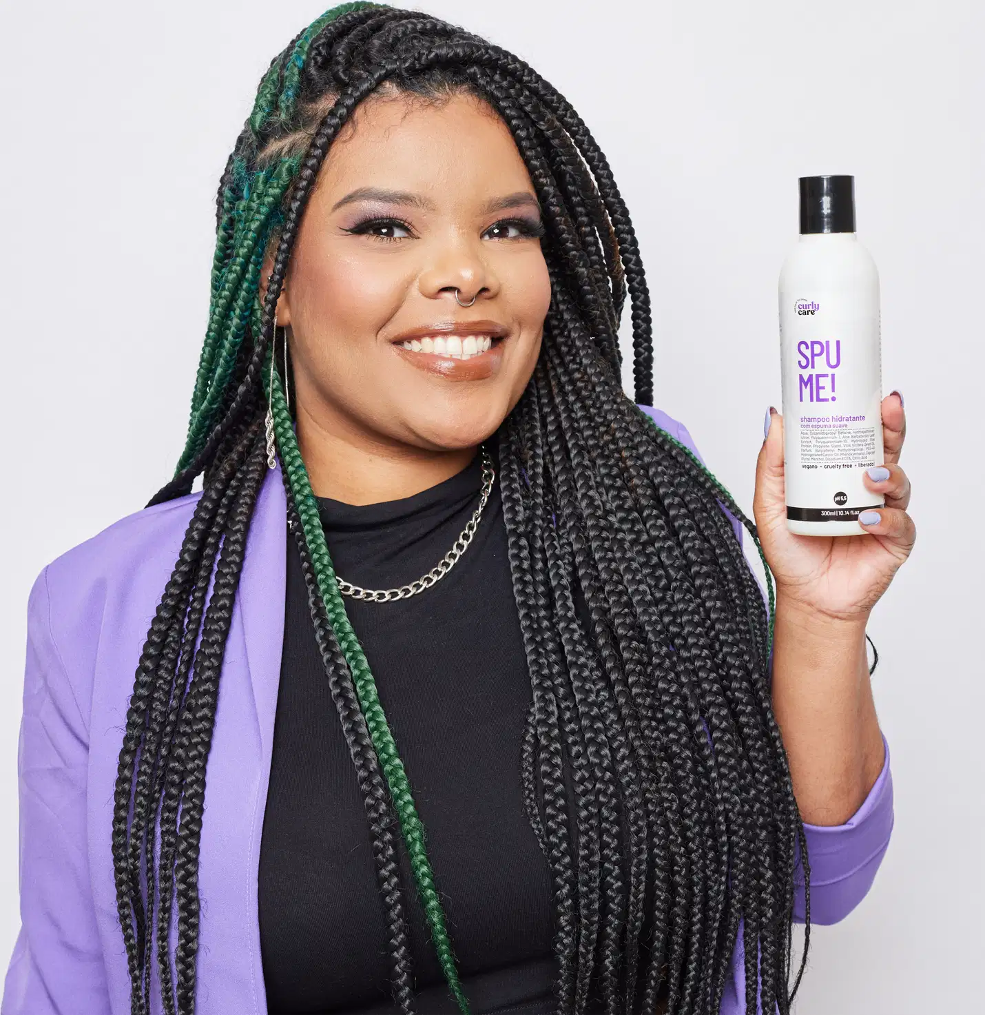 O produto mostrado é um shampoo chamado "Spu Me!". O O frasco está sendo segurado por uma pessoa com longos cabelos negros trançados, que incluem detalhes em verde