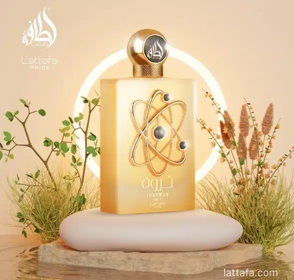 Um item de perfumaria dourado com um símbolo atômico em destaque, posicionado sobre uma superfície de madeira. Ao redor, há plantas verdes e flores secas, criando um ambiente natural e elegante.