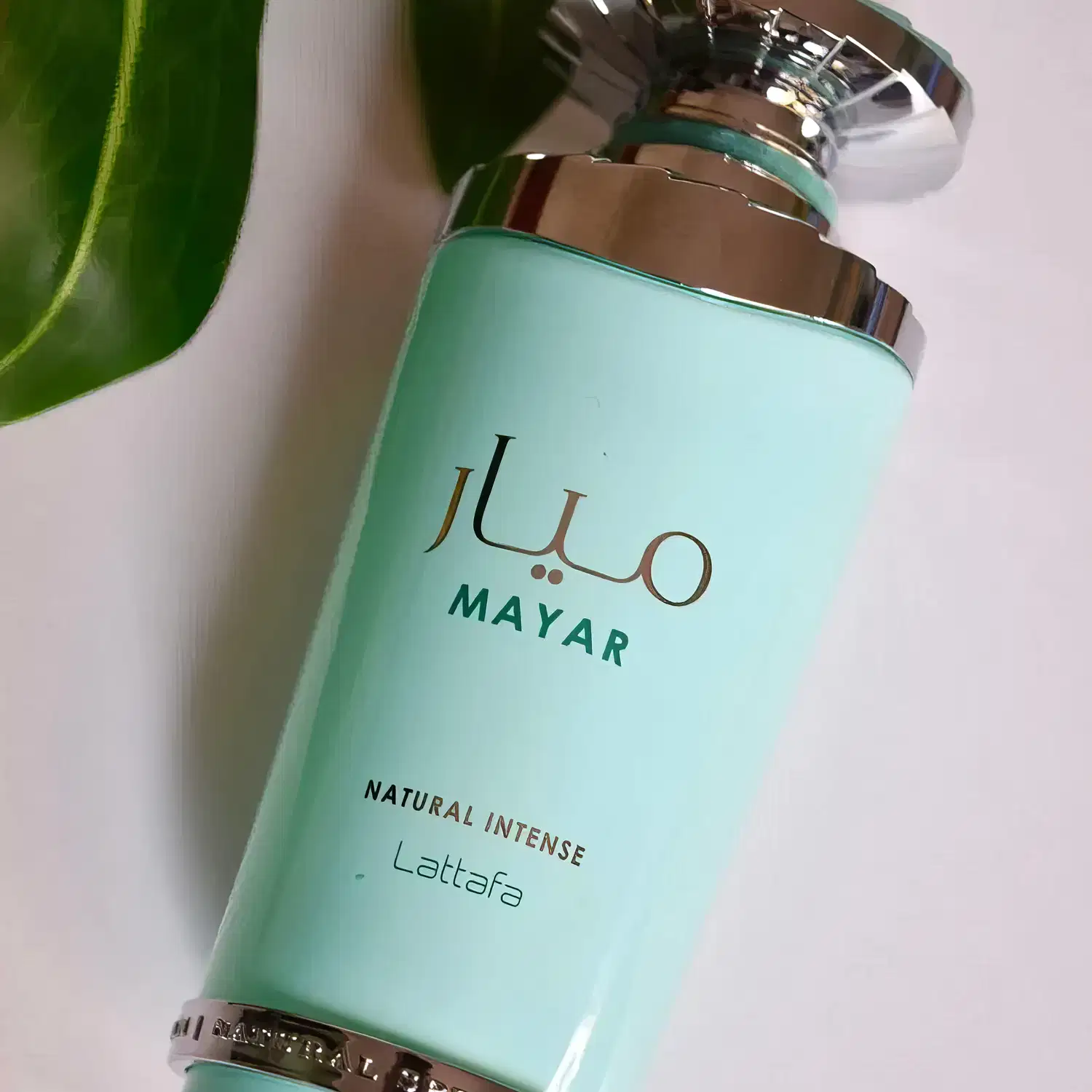 Frasco de item de perfumaria de cor verde-azulada com rótulo exibindo a marca "Lattasfa" e a descrição "Natural Intense Lattafa". O frasco possui um design elegante com detalhes em dourado.