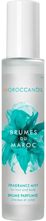 A imagem mostra o produto Moroccanoil Brumes du Maroc 100ml.  O rótulo indica que é um "Fragrance Mist" (Bruma Perfumada). O design do rótulo apresenta folhas estilizadas de tom turquesa sobre um fundo branco, dando uma aparência inspirada na natureza.