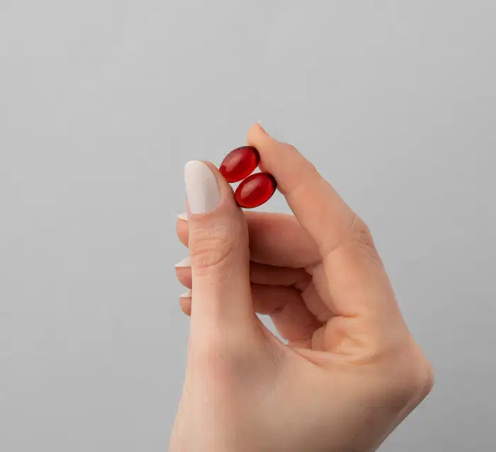 A imagem mostra uma mão segurando duas cápsulas com o dedo polegar e o indicador.
