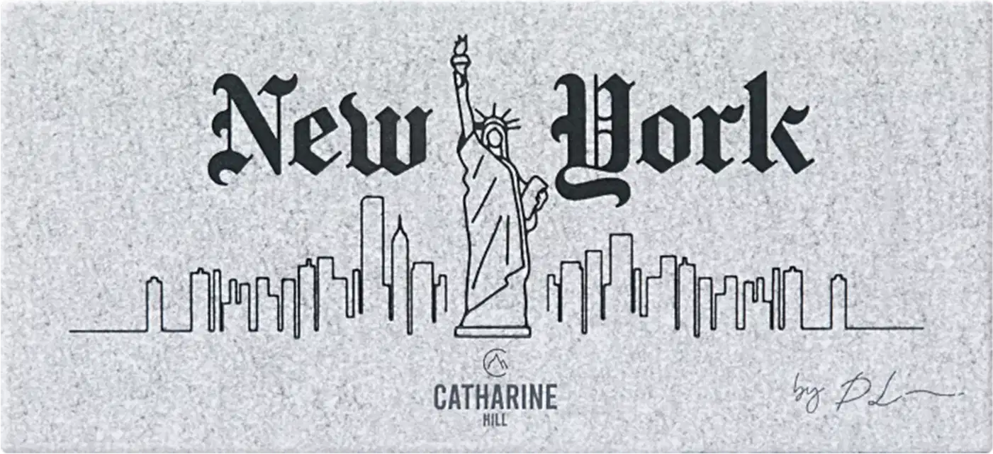 A embalagem fechada mostra a imagem em preto e branco que apresenta o logotipo e o nome "New York" em um estilo de fonte gótica antiga. A imagem inclui um desenho da Estátua da Liberdade e um esboço da skyline de Nova York com vários edifícios.