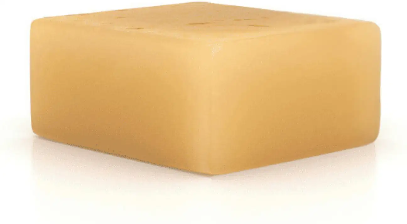 O produto apresentado é um bloco de sabonete de cor bege, um sólido retangular com superfície lisa e uniforme.