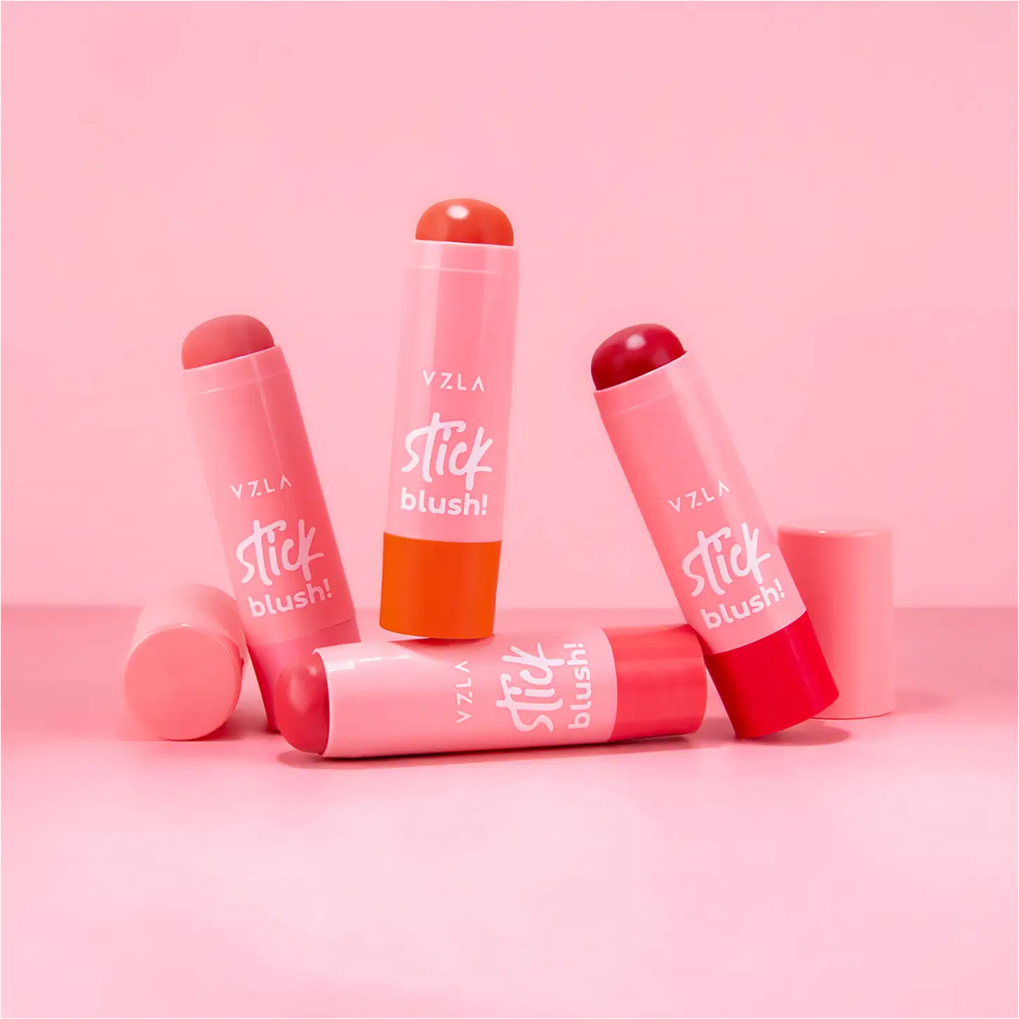 Quatro produtos de maquiagem da marca Vizzela. São blushes em formato de bastão, com embalagens plásticas nas cores rosa claro, rosa escuro e vermelho.