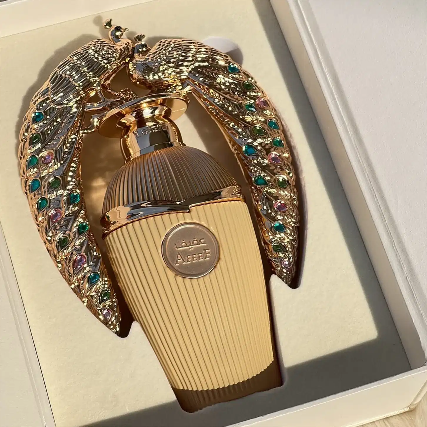 Frasco de perfume dourado da marca Lattafa Perfumes, com detalhes em formato de pássaro ornamentado com pedras coloridas, embalado em uma estrutura decorativa.