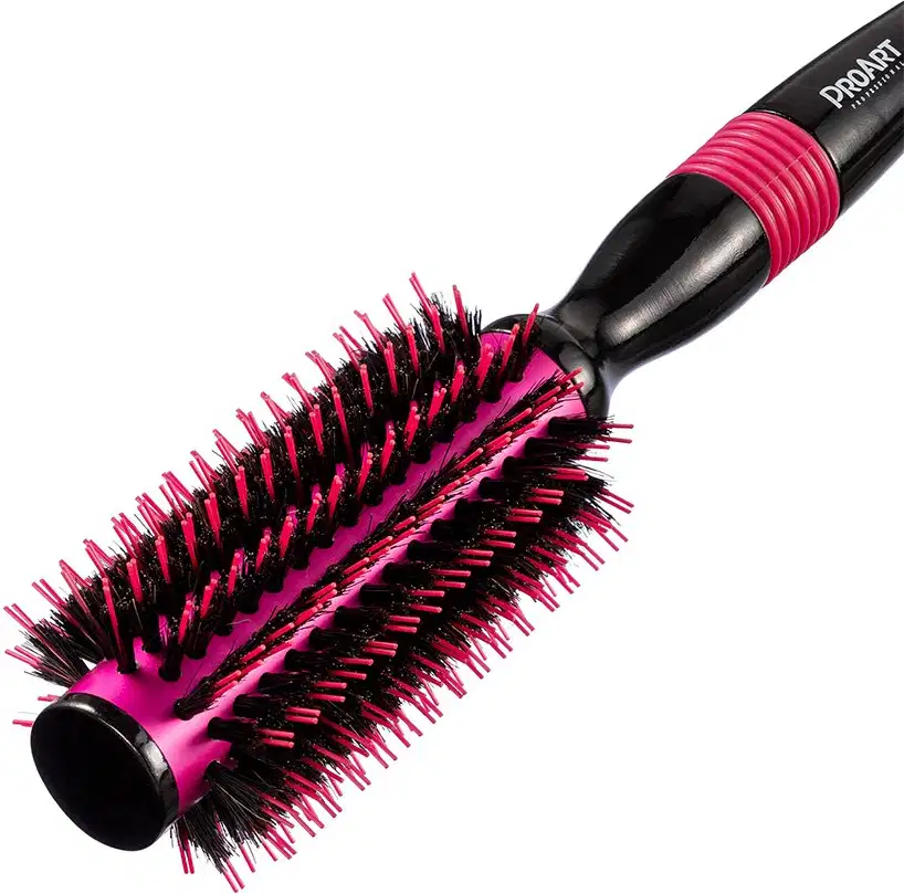 A imagem mostra a escova de cabelo em formato arredondado. Ela possui um corpo preto com cerdas rígidas e densas em tons de rosa vibrante e preto. Design moderno e ergonômico com cabo emborrachado rosa.