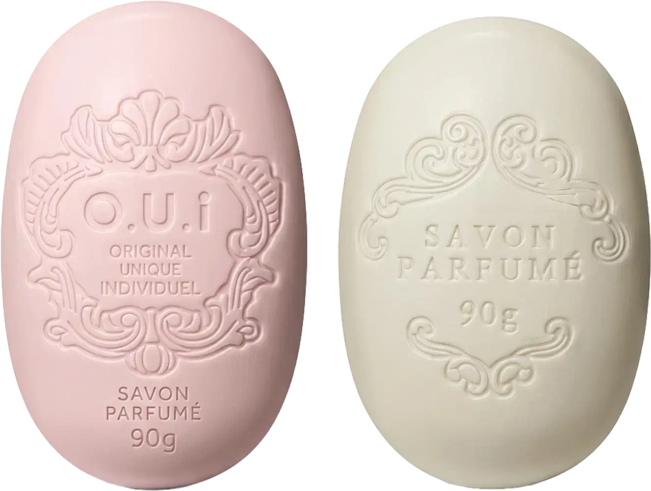 Dois sabonetes O.U.i em formato oval com relevos decorativos. À esquerda, sabonete rosa com inscrição "O.U.i Original Unique Individuel" e "Savon Parfumé 90g". À direita, sabonete bege com texto "Savon Parfumé 90g".