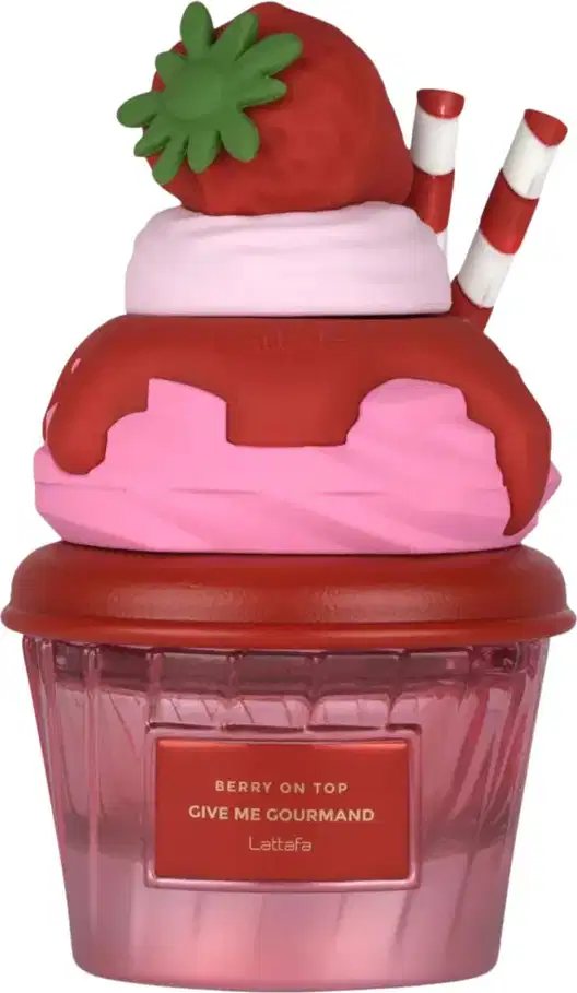 Frasco de perfume em formato de cupcake vermelho e rosa, com tampa em formato de morango verde. Rótulo indica o nome "Berry on Top Give Me Gourmand" da marca Lattafa.