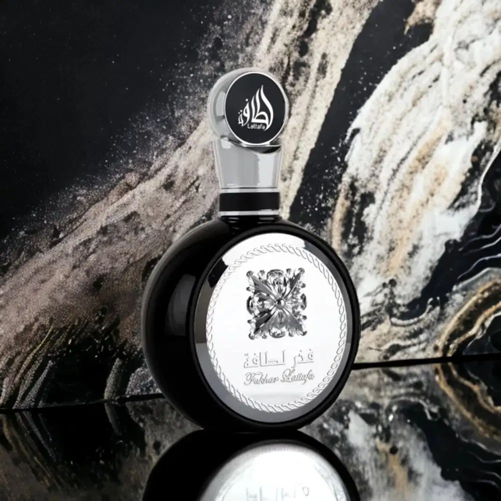 Frasco de perfume Lattafa com design elegante e moderno. Recipiente de vidro transparente com tampa preta e logotipo da marca em destaque. Embalagem com acabamento refinado e detalhes decorativos.