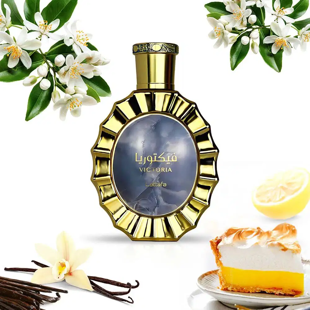 Recipiente dourado de item de perfumaria com rótulo "Victoria" em fundo desfocado. Flores brancas e limão ao redor, com bolo e baunilha no primeiro plano, sugerindo um ambiente elegante e refinado.