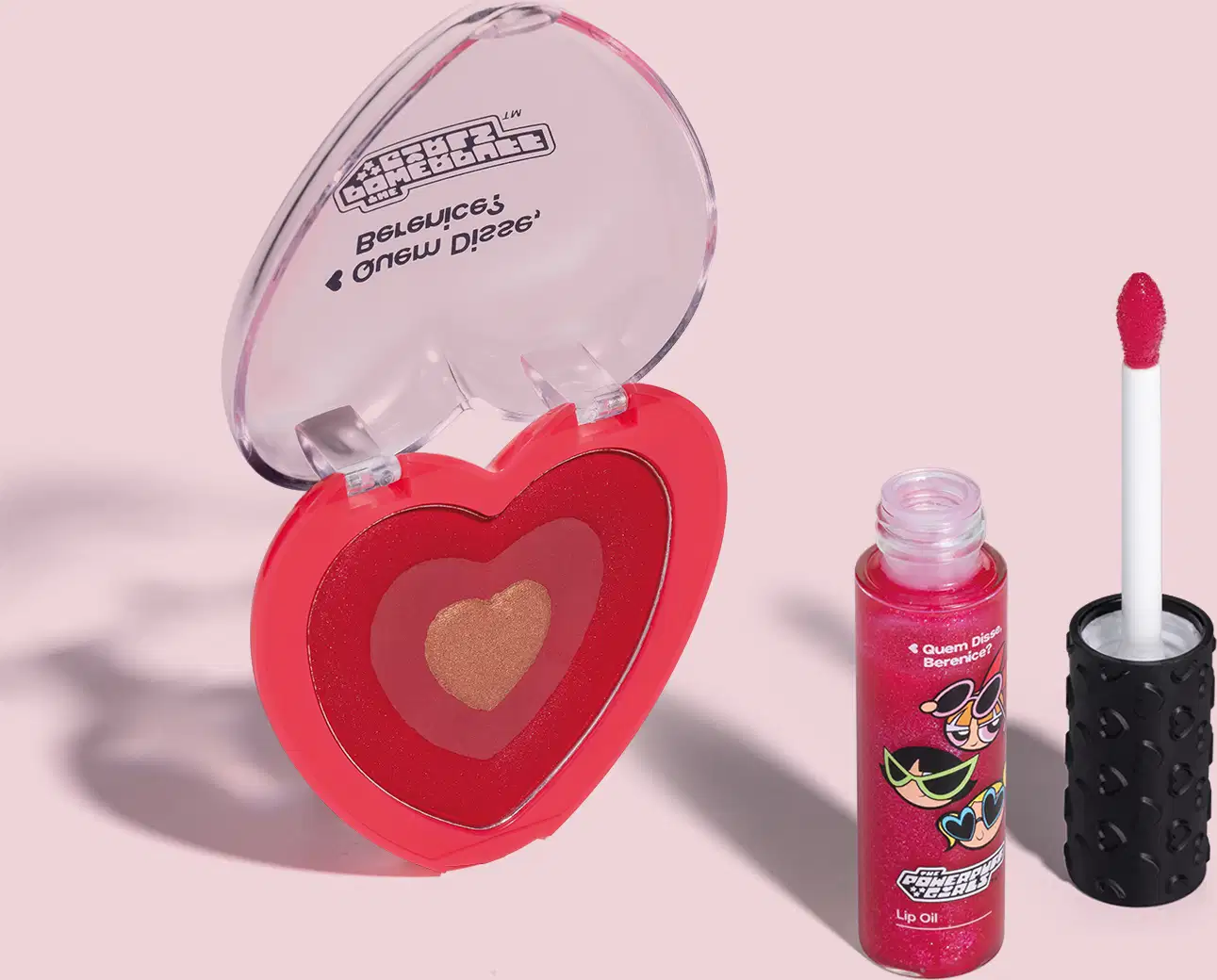 Dois itens da marca Meninas Superpoderosas Quem Disse, Berenice?: um lip oil vermelho em embalagem transparente com personagens e um blush compacto em formato de coração vermelho com tampa transparente em fundo lilás com leve sombreado.