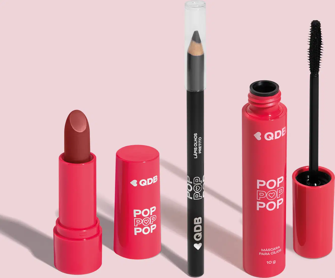 Imagem de um batom Marrom Nude Avelã em embalagem rosa e letras brancas, um lápis preto para olhos com tampa transparente e uma máscara para cílios em embalagem e tampa rosa com aplicador na cor preta. O fundo da imagem é neutro com sombreado.