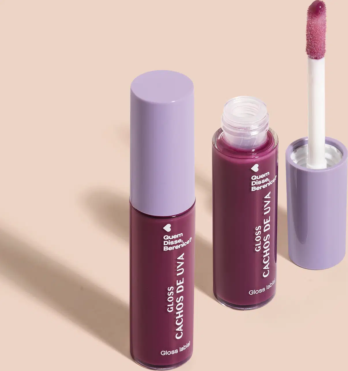 Imagem de combo com dois frascos de 10ml contendo gloss labial Cachos de Uva QDB E Cuide-se Bem Quem Disse, Berenice?. A embalagem é transparente com conteúdo roxo, tampa cinza e aplicador macio na cor roxa. O fundo é bege com leve sombreado.
