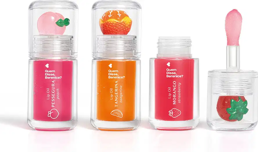 Imagem do Combo Lip Oil Quem Disse, Berenice? com as cores Vermelho Morango, Rosa Fúcsia Pessegura e Coral Tangerina. As embalagens são transparentes com aplicador macio e trazem a fruta correspondente decorando a tampa.