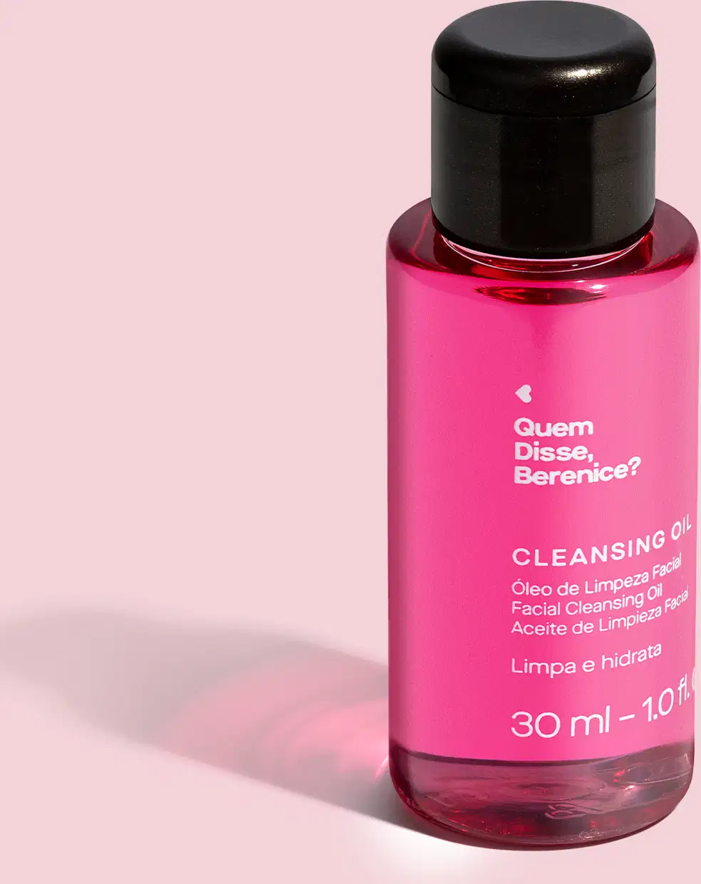 Imagem de frasco transparente e tampa preta contendo um líquido rosa com rótulo branco "Quem disse, Berenice? Cleansing Oil" em preto, trazendo 30 ml de óleo de limpeza facial. Ele está em fundo em tom de rosa bem claro e um leve sombreado da embalagem.