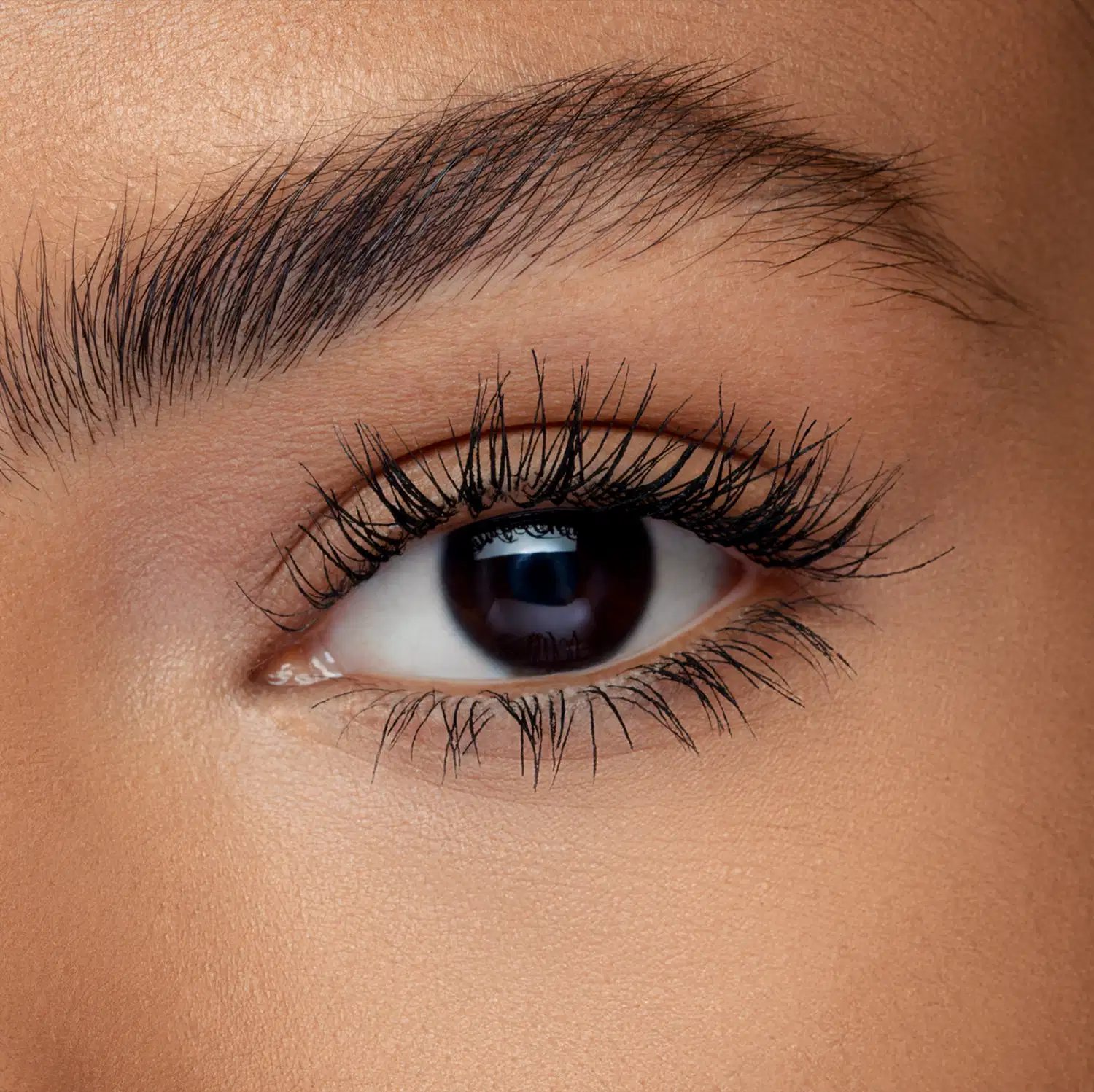 Close-up de um olho feminino com cílios longos e escuros. O olho possui uma íris escura e brilhante, com a pálpebra superior destacada por uma maquiagem preta usando a máscara de cílios Big Bang Explosão de Volume Quem Disse, Berenice?.