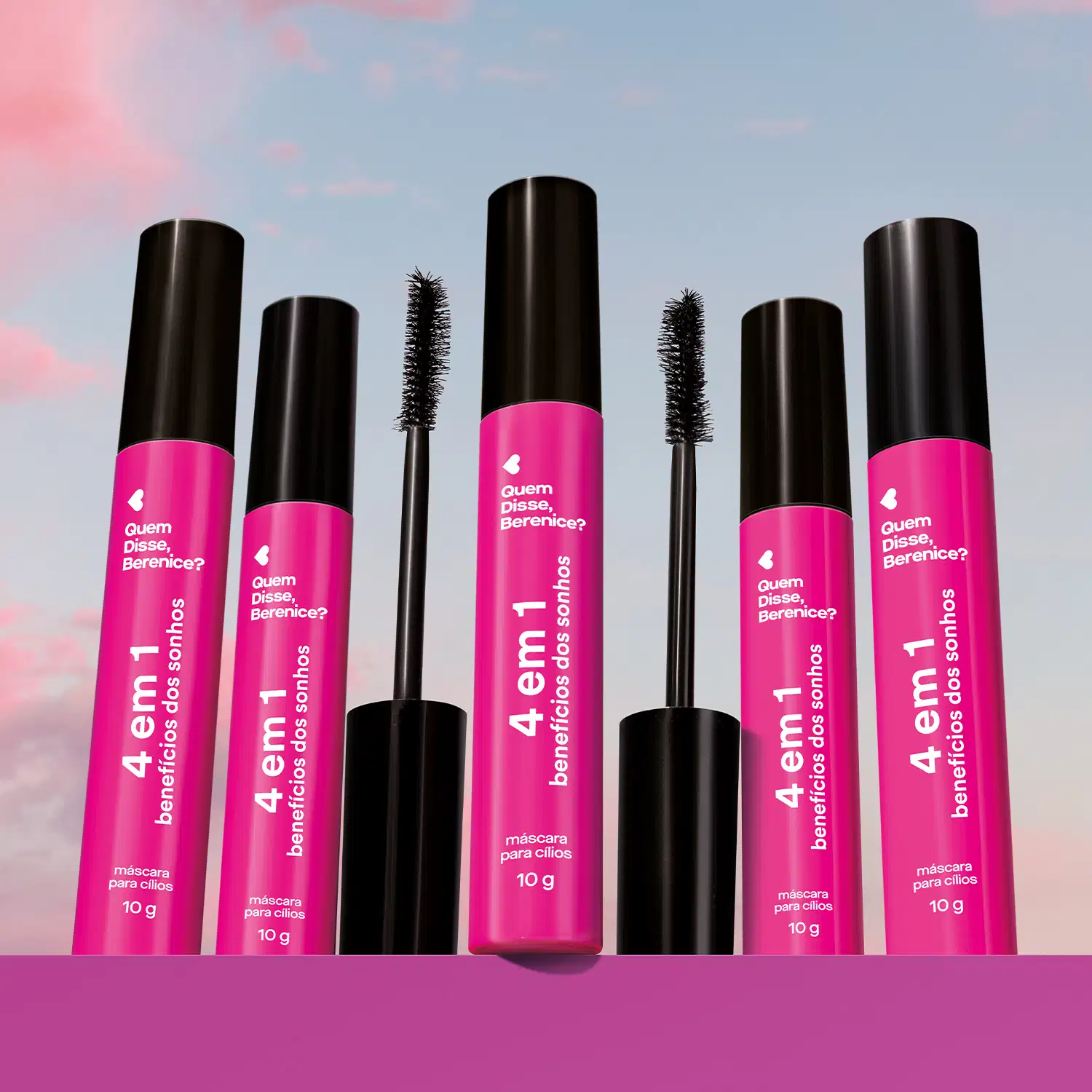 Diversas embalagens de máscaras para cílios 4 Em 1 Benefícios Dos Sonhos Quem Disse, Berenice? na cor rosa com tampa preta em superfície rosa e fundo azul claro.